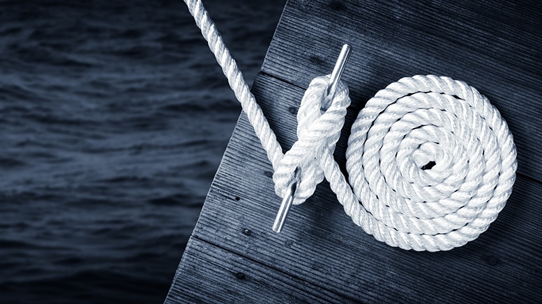 White rope coiled on a dark wooden dock by water