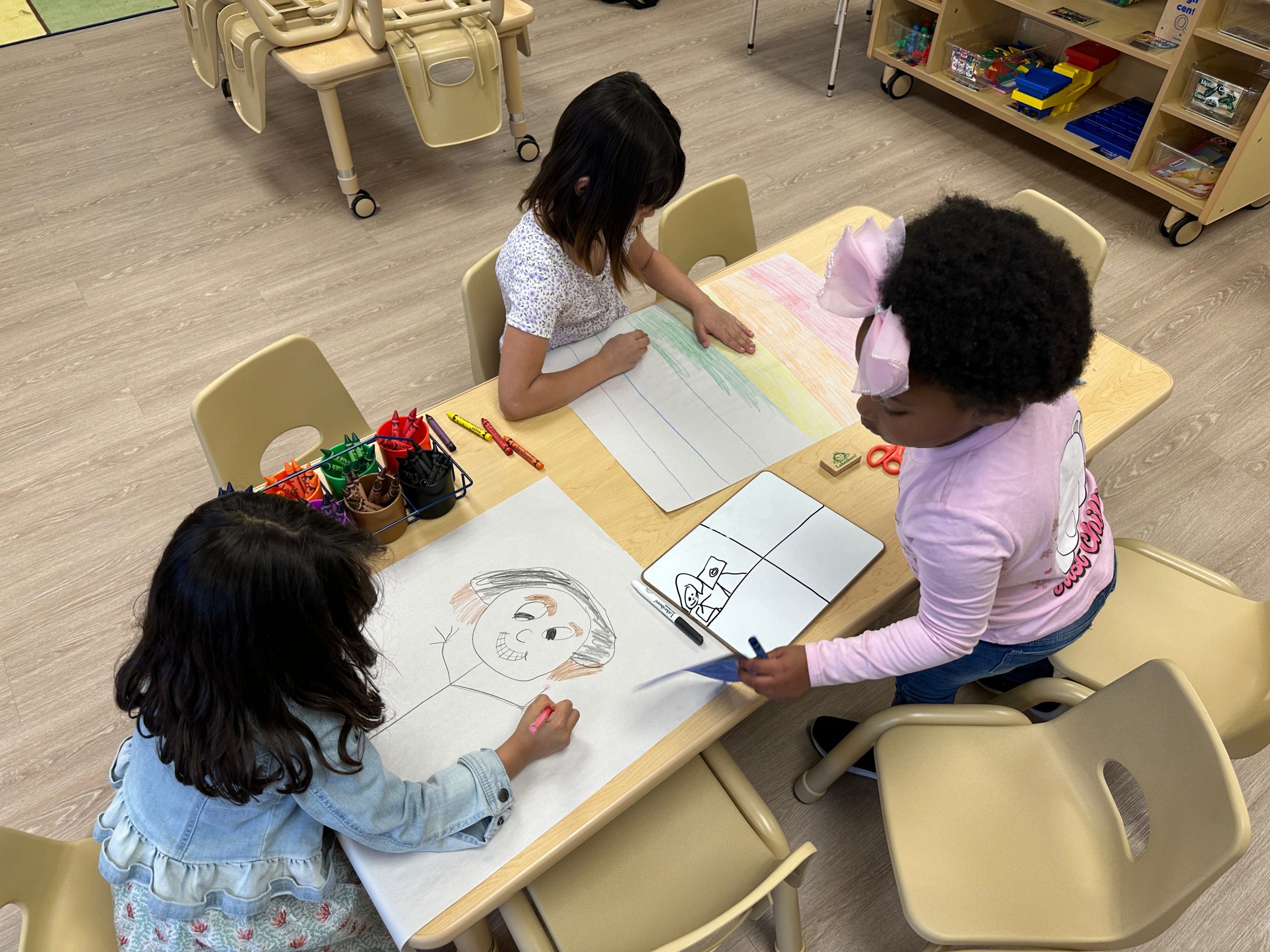 Children at a small classroom table drawing on paper