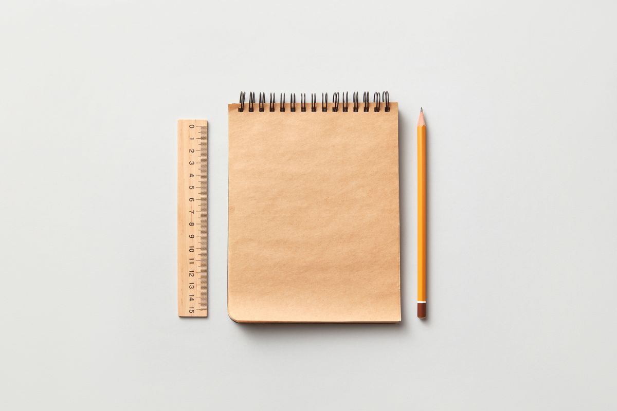 A wooden ruler, kraft-paper notebook, and pencil arranged on a neutral surface